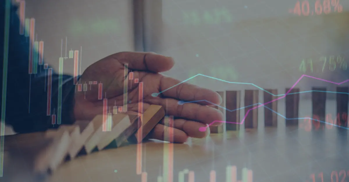 An image of domino blocks with a hand in the middle of it with online trading charts to represent risk management in online trading